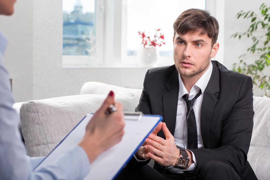 young man in a business suit talks with therapist about the 5 benefits of a men's addiction treatment program